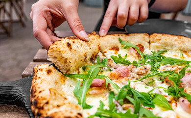 woman Hand takes a slice of meat Pizza with Mozzarella cheese, ham, bacon, Spices and chicken in cafe outdoor