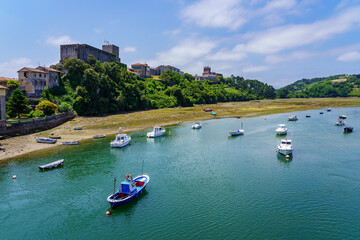Fototapeta premium Sea estuary under the medieval castle with small boats anchored. San Vicente de la Barquera.