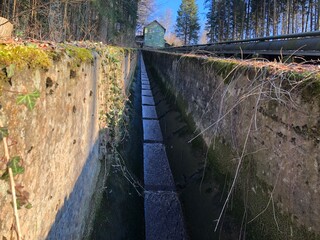 Fluss der einen Hang in einer Rinne runterläuft in einem Wald mit Himmel.
