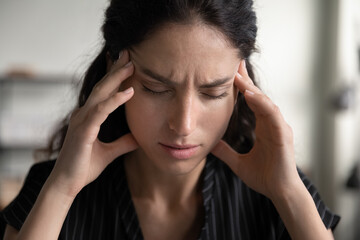 Close up of unhealthy millennial Caucasian woman touch temples have migraine or headache. Unwell tired young female suffer from blurry vision or dizziness overwhelmed with work. Overwork concept.