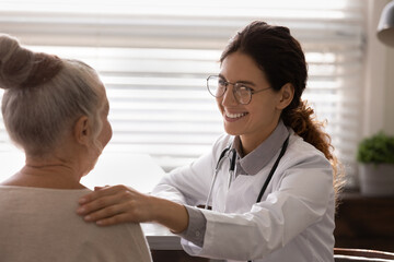 Smiling young woman doctor touch support old woman patient at consultation in hospital. Happy...