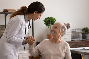 Smiling young Caucasian female doctor hold old woman patient hand support and comfort in hospital. Caring nurse caress happy optimistic mature client at consultation. Geriatrics, healthcare concept.