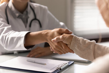 Crop close up of female doctor and mature patient shake hands get acquainted greet at meeting in hospital. Woman GP handshake client close health insurance deal. Geriatrics, healthcare concept.