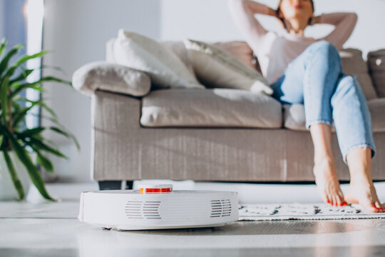 Woman Relaxing On Sofa While Robot Vacuum Cleaner Doing Housework