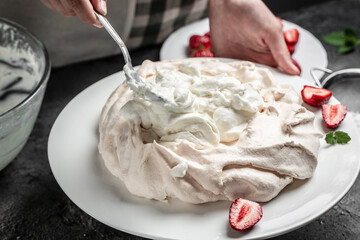 Baker decorating fresh delicious homemade Pavlova cake meringue cake with whipped cream and strawberries. culinary, bakery, food and people concept.