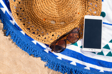 Straw hat, sunglasses and a phone on a towel on the beach. Close-up. - 441721439