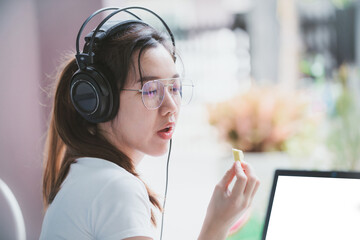 Teenage students wear headphones while studying online comfortably at home. Or company employees sit and work online at home. Eat snack or fruit while studying or working in front of the laptop screen