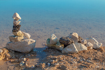 Stones stacked on the shore of a turquoise lake on a bright sunny day. - 441722801