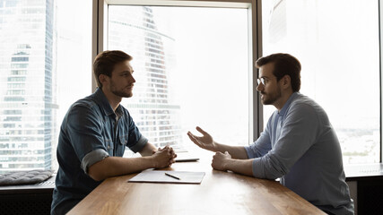 Concentrated young male vacancy candidate asking questions about job position to confident employer...