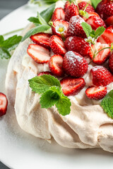 Australian dessert Pavlova cake meringue with whipped cream, fresh strawberrie and mint. Food recipe background. Close up