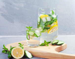 Delicious cold summer lemonade with cucumber and mint in stone jars on a light slate, stone or concrete background.