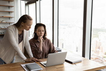Concentrated smart young female supervisor boss leader instructing or helping colleague with...