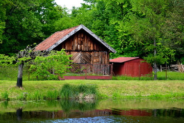 A view of a small wooden shack, hut or house made entirely out of logs and planks with an angled roof and a small storage unit nearby located next to the bank of a vast yet shallow river in Poland