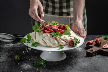 Baker decorating fresh delicious homemade Pavlova cake with fresh strawberries and whipped cream. culinary, bakery, food and people concept
