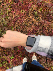 Square smart watch with a pink strap on a female hand against a background of bright autumn foliage