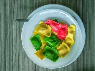 White plate of multi-colored ravioli is standing on a wooden table. Close-up.