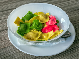 White plate of multi-colored ravioli is standing on a wooden table. Close-up.