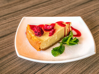 White plate with a cheesecake is standing on a wooden table. Close-up.
