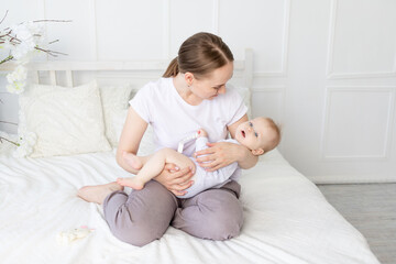 happy mom holds baby in her arms with a rodent in her mouth on a white bed with cotton bedding at home