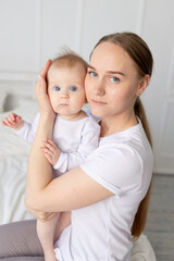 portrait of a mother with a baby in her arms gently embracing him on a white bed at home, mother's love