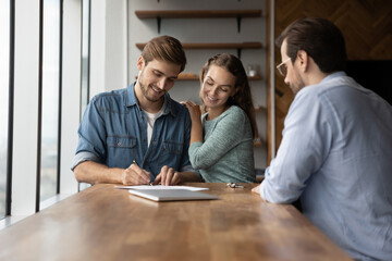 Affectionate loving young happy married couple signing agreement document with professional...