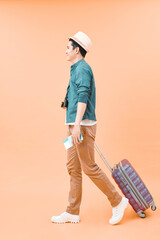 Happy asian male traveler walking with suitcase against color background