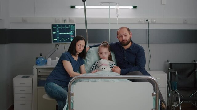 Portrait of worried family looking into camera in hospital ward during therapy consultation waiting medical expertise. Sick girl child patient resting in bed wearing oxygen nasal tube for recovery