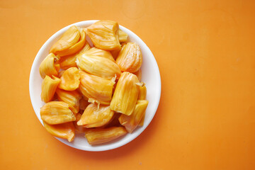 top view of slice of jackfruits in a bowl on orange background .
