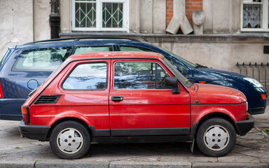 Two subcompact cars are parked on the sidewalk near a high-rise building in Warsaw, Poland.