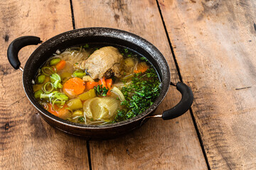 Zupa z kurczaka z warzywami podana w czarnym garnku na drewnianym tle.