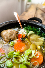 Zupa z kurczaka z warzywami podana w czarnym garnku na drewnianym tle.