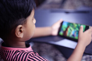 Happy young boy watching cartoon in a mobile phone , Side view of kid watching videos