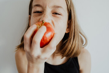 Delighted kid biting apple against white wall