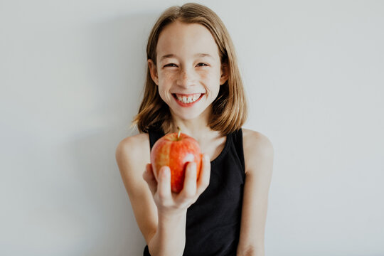 Delighted kid biting apple against white wall