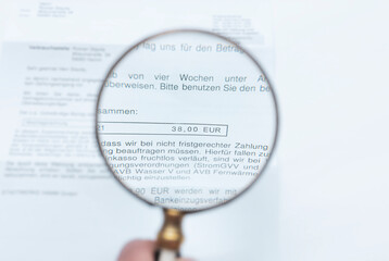 A man looks through a magnifying glass at an invoice.