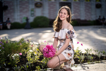 cheerful girl in a light summer dress against the background of a city park