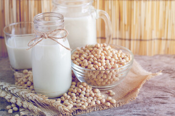 Closed up delicious homemade soybean milk in glass bottle with some seeds in glass bowl with dry wheat ear on wooden background in soft light vintage tone