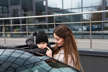 smiling woman touching cheek of baby boy near car outdoors