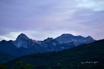 Fototapeta premium Scenic view of the Pania Mountain, in the Apuan Alps, illuminated by the warm light of the sunset from the Garfagnana, in the high Tuscany, on a summer evening with some clouds.