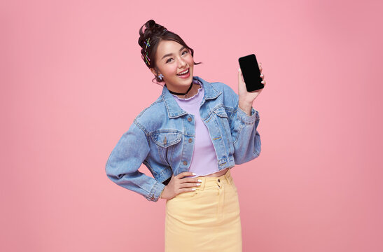 Happy Young Asian Woman Showing At Blank Screen Mobile Phone And Hand Gesture Success Isolated Over Pink Background.