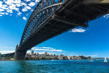 Fototapeta premium Sydney bay with yachts in the water passing under heavy metal bridge.