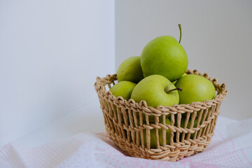 Wicker natural basket with green apples on a white and gray background. White and pink cotton textile napkin towel. Simple organic food view. Empty space for text or design. Template for business.