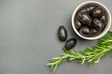Black olives. Bella di cerignola Italian olives. Colored olives and a sprig of rosemary lie on a black stone countertop. Culinary banner or poster for advertising with place for text