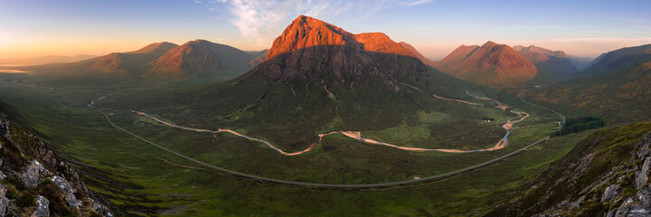 Ultra wide panoramic view of mountain range at sunrise. The Buachaille, Glencoe, Scottish Highlands. A meandering river and long curving road can be seen in foreground of landscape. - Powered by Adobe