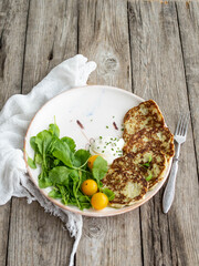 Zucchini pancakes with arugula and yellow cherry tomatoes on wood background. Copy space, close up.