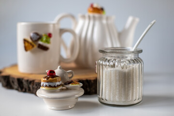 Sugar in a transparent jar. White utensils for tea drinking. The decor on the dishes is sweets. Cup, sugar bowl and teapot. Good morning. Screensaver wallpaper