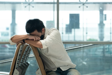 Airport lounge and people waiting for boarding. Body of male on foreground sleeping on his luggage lying in chair. 