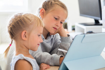 A little preschooler girls watches cartoons on a tablet in a network room, distance education during a pandemic, the children learns high technologies