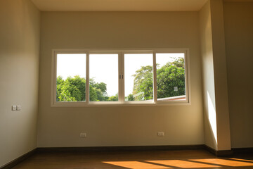 white wall in new house. wooden laminate floor in living room. big square windows clear glass green tree background.