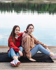 Two young caucasian young women sitting on the pier near lake